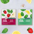 Twee theeverpakkingen van LiveFresh – links „Fruchtenthee Wild Berry“ met aardbeien en appel, rechts „Groene thee Lemon & Mint“ met schijfjes citroen en muntblaadjes; versierd met bijpassend fruit en blaadjes.