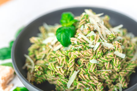 Schüssel mit grüner Pasta, verfeinert mit frisch geriebenem Parmesan und dekoriert mit Basilikumblättern.