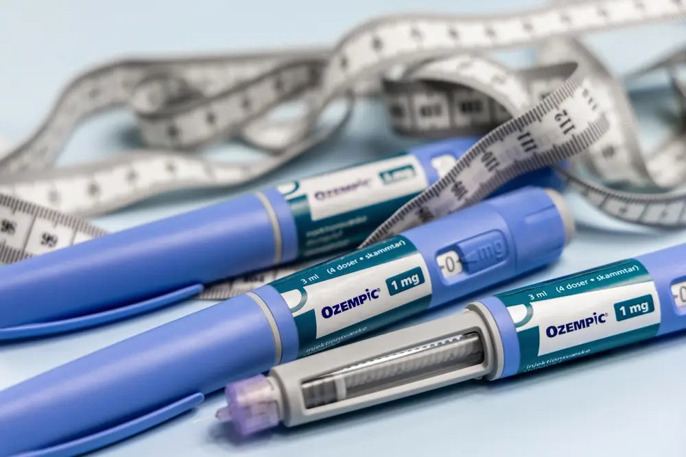 Mehrere blaue Ozempic Pens mit Dosierungseinheit, daneben ein Maßband als Symbol für Gewichtsabnahme und die Anwendung von Ozempic als Abnehmspritze.