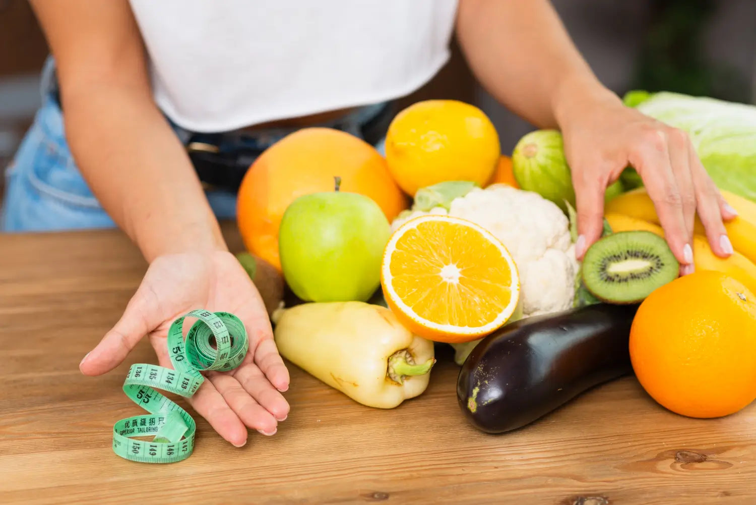 Person hält ein grünes Maßband neben frischem Obst und Gemüse wie Orange, Kiwi und Apfel, was auf eine gesunde Ernährung zur Anregung des Stoffwechsels hinweist.