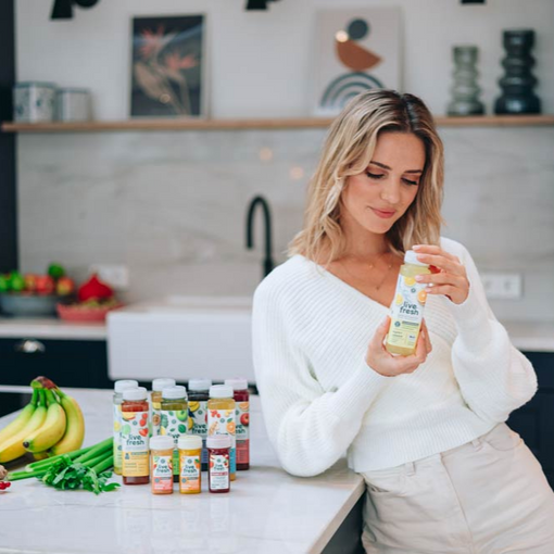 Een jonge vrouw staat in de keuken met LiveFresh sapjes naast haar en een Happy Lemon sapje in haar hand. 