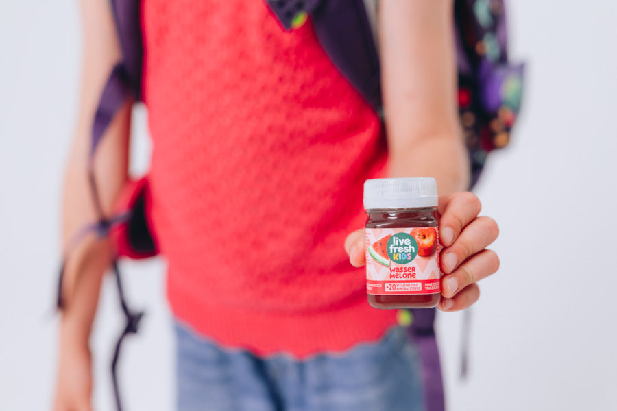 Een kind met een schooltas houdt een LiveFresh Kids Shot Watermeloen omhoog.