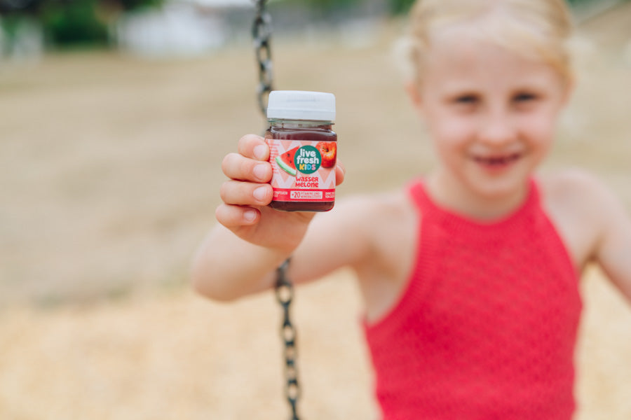 Een meisje presenteert een LiveFresh Kids Shot met watermeloensmaak op een speelplaats.