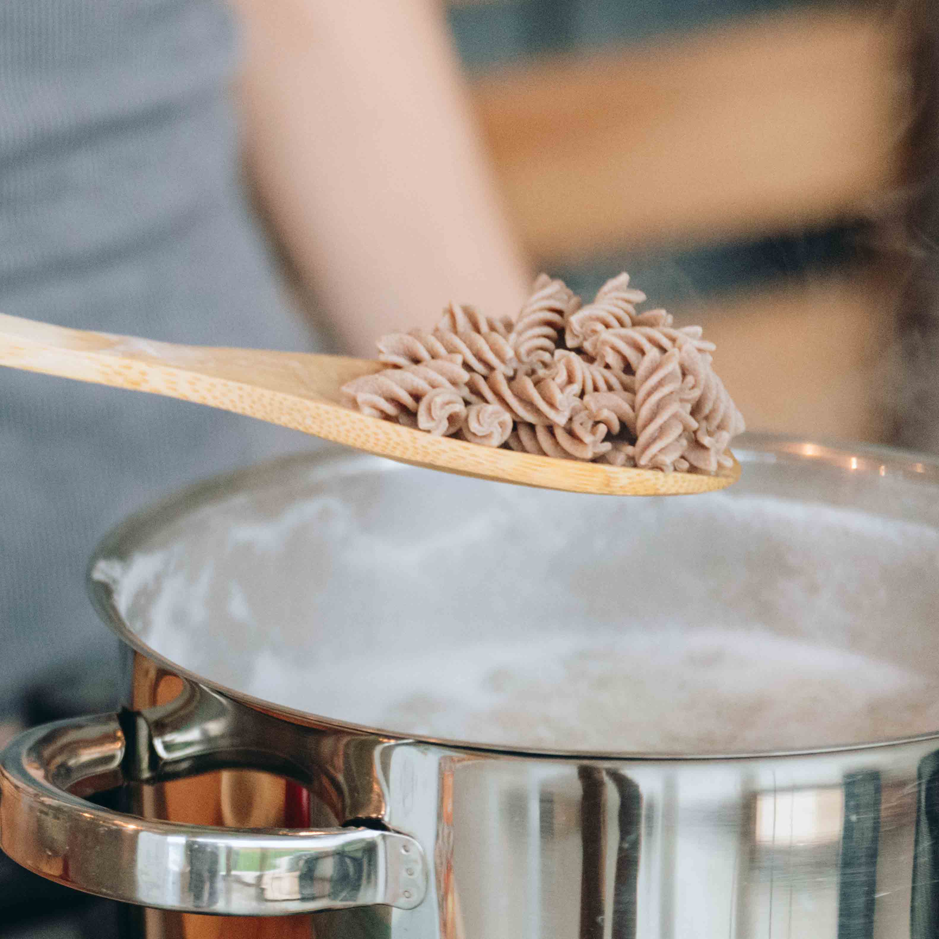 Holzlöffel hebt dampfende High Protein Fusilli aus einem Topf, hervorhebend die einfache Zubereitung der proteinnudeln.