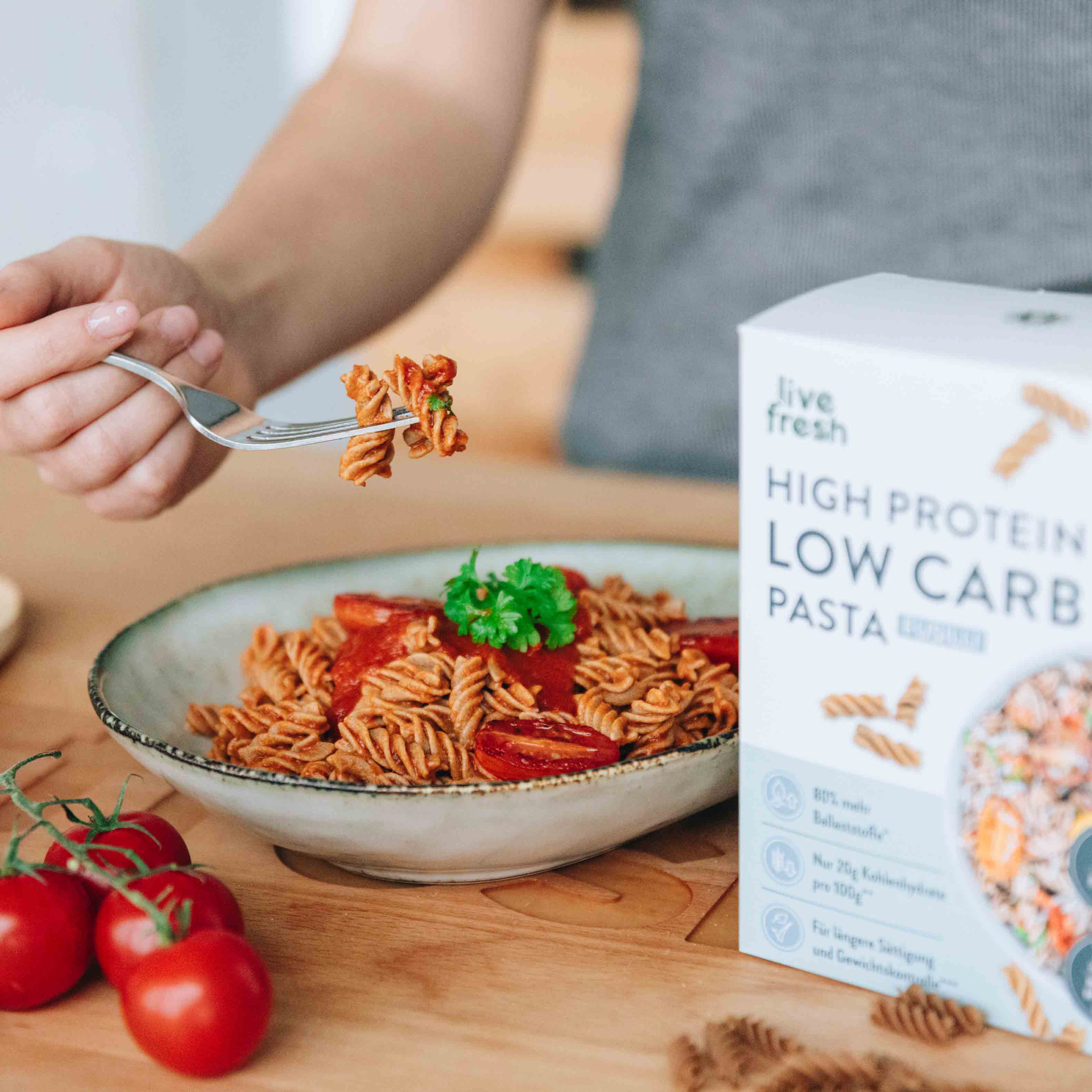 Eine Hand hält eine Gabel mit Low Carb Fusilli über einem Teller, serviert mit Tomatensauce und frischen Tomaten, unterstreicht die Vielseitigkeit der low carb nudeln.