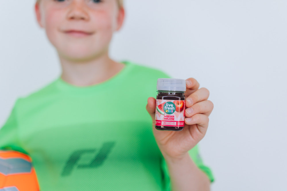 Een jongen in een groen sportshirt houdt een LiveFresh Kids Shot met watermeloensmaak vast.