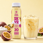 Live Fresh Skyr Protein Drink Maracuja neben einem Glas mit eisgekühltem cremigem Maracujadrink. Auf der Verpackung steht "live fresh SKYR PROTEIN DRINK MARACUJA MIT KOLLAGEN 30 GR. PROTEIN HIGH PROTEIN LOWER CARB NO ADDED SUGAR". Aufgeschnittene Maracujas und eine Schale mit cremigem Skyr stehen daneben.