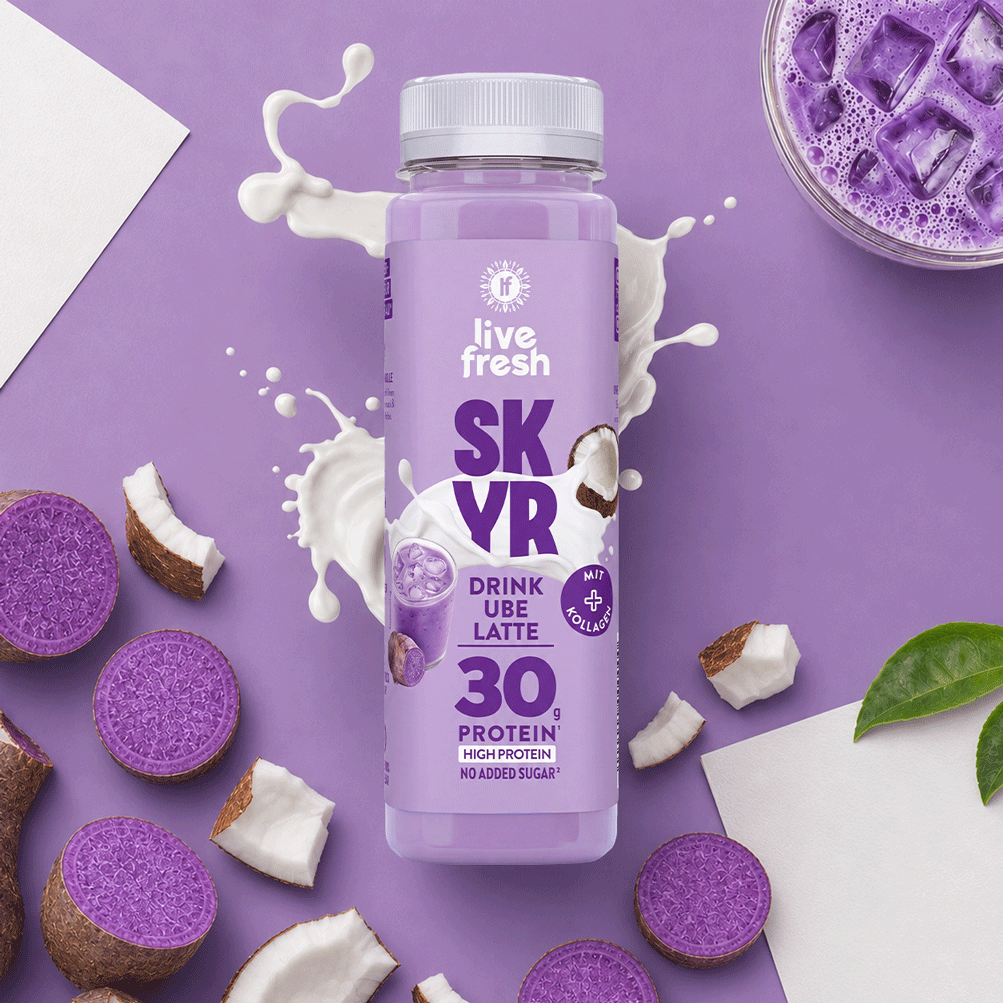 Ube Latte Skyr Drink von LiveFresh auf lila Hintergrund mit 30g Protein Label. Daneben Kokostückchen und offene Ube Knollen. Außerdem Milch und ein Glas Ube Latte mit Eiswürfel. 