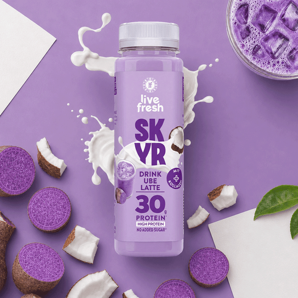 Ube Latte Skyr Drink von LiveFresh auf lila Hintergrund mit 30g Protein Label. Daneben Kokostückchen und offene Ube Knollen. Außerdem Milch und ein Glas Ube Latte mit Eiswürfel. 