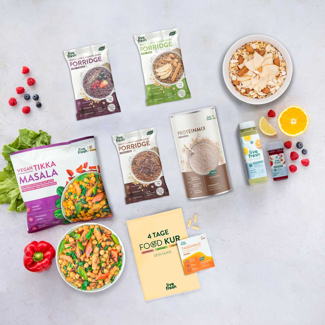 Flatlay mit verschiedenen Produkten aus der Tage-Foodkur/Abnehmbundles von LiveFresh: Porridges, Proteinmix, Tikka Masala, Säfte, Shots, ein Foodkur-Guide und Vitaminpräparate. Umgeben von frischem Obst und Gemüse.