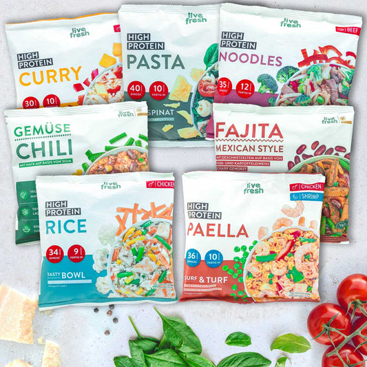 Auswahl an LiveFresh High Protein Bowls in verschiedenen Sorten wie Curry, Pasta, Noodles, Gemüse Chili, Fajita, Rice und Paella, dekorativ angerichtet mit frischen Kräutern, Tomaten und Käse auf hellem Untergrund.