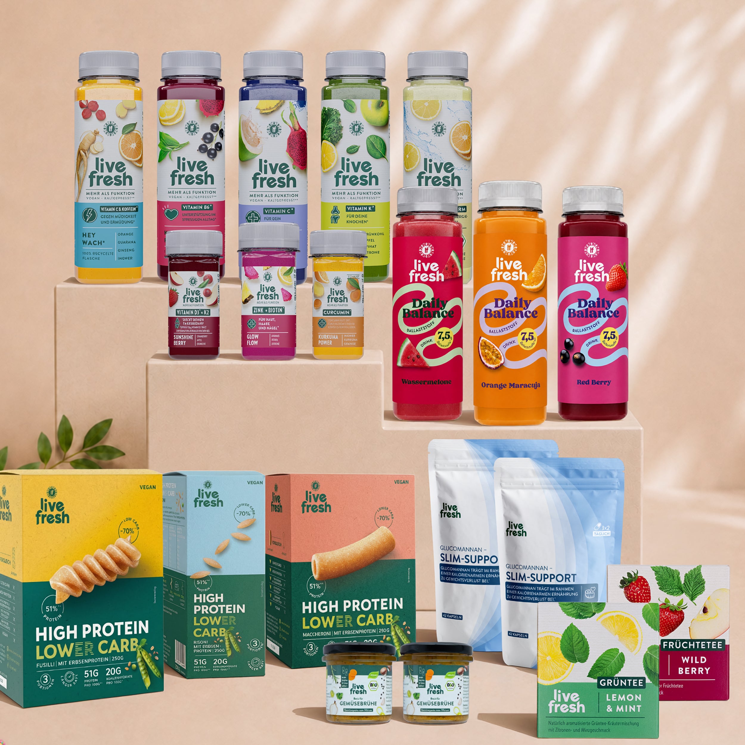 Umfangreiche Auswahl an LiveFresh Produkten auf gestuften Podesten mit Daily Balance Ballaststoffdrinks in mehreren Sorten, funktionellen Getränken, High Protein Lower Carb Pasta, Glucomannan Slim Support, Gemüsebrühe und Tee. Das Sortiment veranschaulicht eine Balance Kur mit Schwerpunkt auf ballaststoffreicher Ernährung und alltagstauglicher Ergänzung.