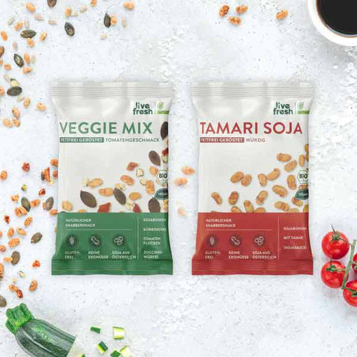 Zwei Packungen „Live Fresh“ Snacks: den „Veggie Mix“ mit Tomatengeschmack und „Tamari Soja“. Beide Snacks sind fettfrei geröstet und bio-zertifiziert. Der „Veggie Mix“ enthält Zutaten wie Kürbiskerne, Tomatenflocken und Zucchiniwürfel, während der „Tamari Soja“ würzige Sojabohnen mit Tamari (Sojasauce) bietet. Beide Produkte sind glutenfrei, erdnussfrei und bestehen aus Sojabohnen aus Österreich. 