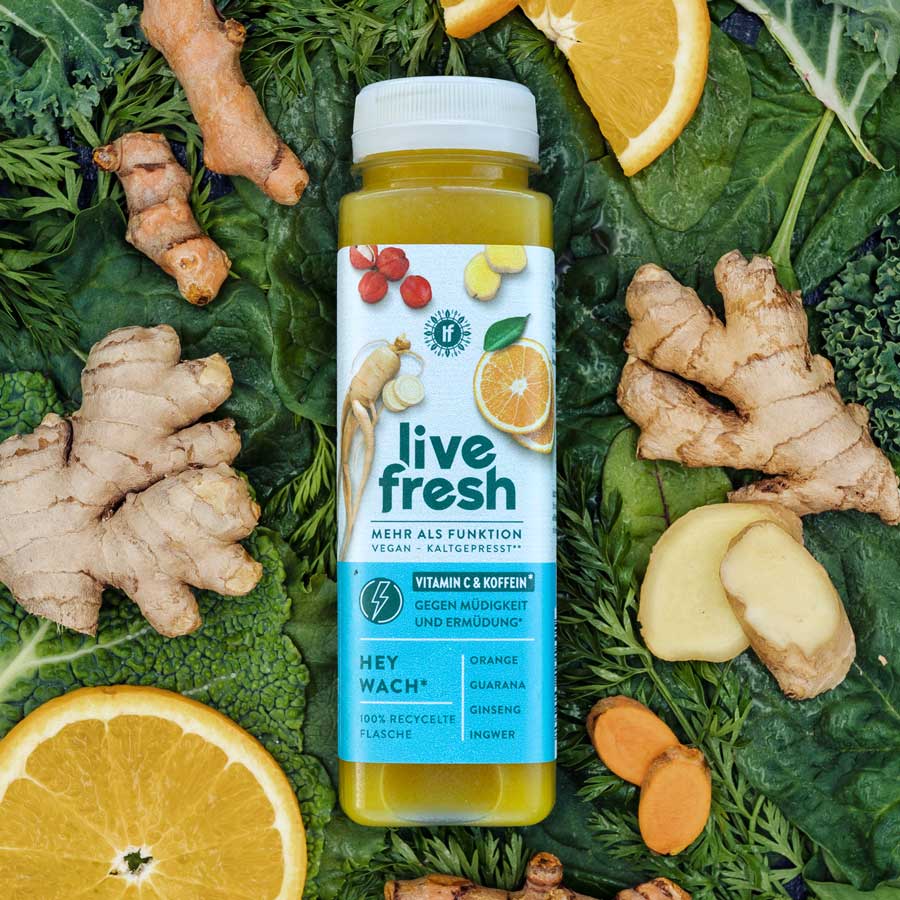 Eine Flasche „Live Fresh Hey Wach“ Saft, umgeben von frischen Zutaten wie Ingwer, Kurkuma, Orangen und Spinatblättern. Der Saft ist vegan, kaltgepresst und enthält Vitamin C sowie Koffein, um gegen Müdigkeit und Erschöpfung zu wirken. Zu den Hauptzutaten gehören Orange, Guarana, Ginseng und Ingwer. Die Flasche besteht aus 100% recyceltem Material, was zusätzlich die nachhaltige Ausrichtung des Produkts betont.