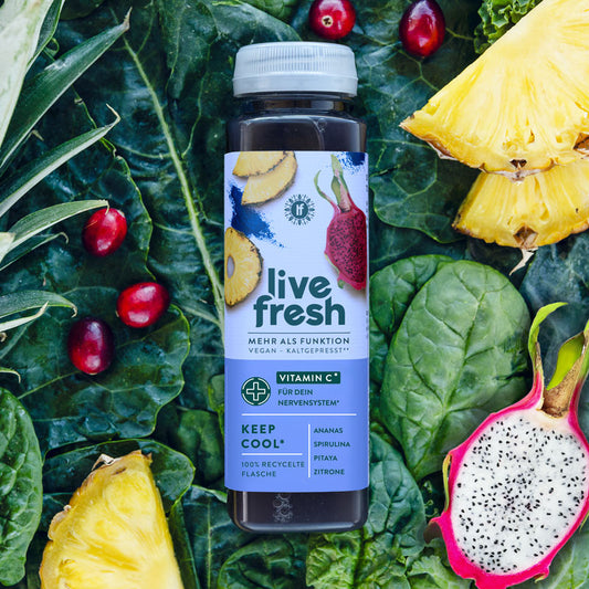 Eine Flasche „Live Fresh Keep Cool“ Saft, umgeben von frischen Zutaten wie Ananas, Pitaya (Drachenfrucht), Zitronen und Spinatblättern. Der Saft ist vegan, kaltgepresst und enthält Vitamin C, das zur Unterstützung des Nervensystems beiträgt. Zu den Hauptzutaten gehören Ananas, Spirulina, Pitaya und Zitrone. Die Flasche besteht aus 100% recyceltem Material, was zusätzlich die Nachhaltigkeit des Produkts unterstreicht.