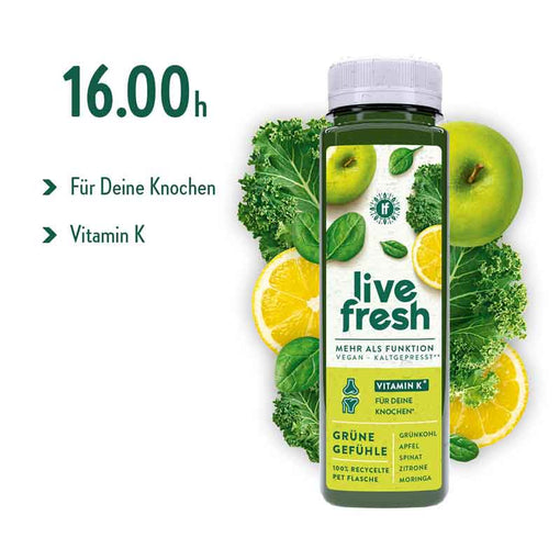 Eine Flasche des veganen, kaltgepressten Safts „Live Fresh“, umgeben von frischen Zutaten wie grünem Apfel, Grünkohl und Zitronenscheiben. Auf der Flasche wird Vitamin K hervorgehoben mit dem Hinweis „Für Deine Knochen“. Die Sorte „Grüne Gefühle“ enthält Grünkohl, Apfel, Spinat, Zitrone und Moringa. Links im Bild steht groß die Uhrzeit „16.00h“, was als empfohlene Konsumzeit dient.