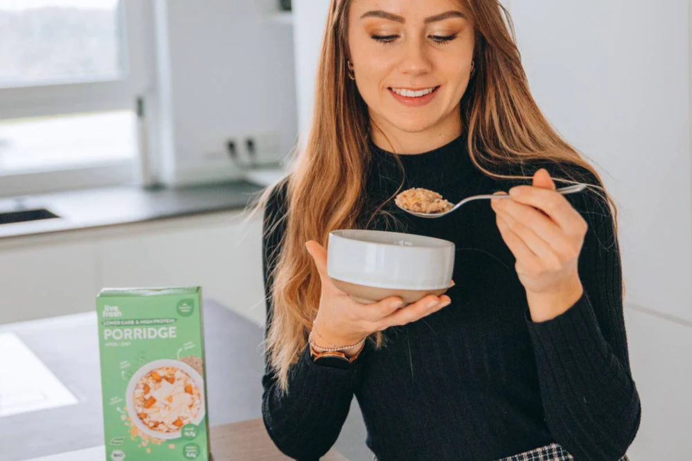 Es ist eine Person zu sehen, die einen Löffel voll Porridge isst. Neben ihr steht eine Packung Live Fresh Porridge mit der Aufschrift "Lower Carb & High Protein". Die Szene vermittelt ein Gefühl von gesundem Start in den Tag und bewusster Ernährung, perfekt für ein energiegeladenes Frühstück.