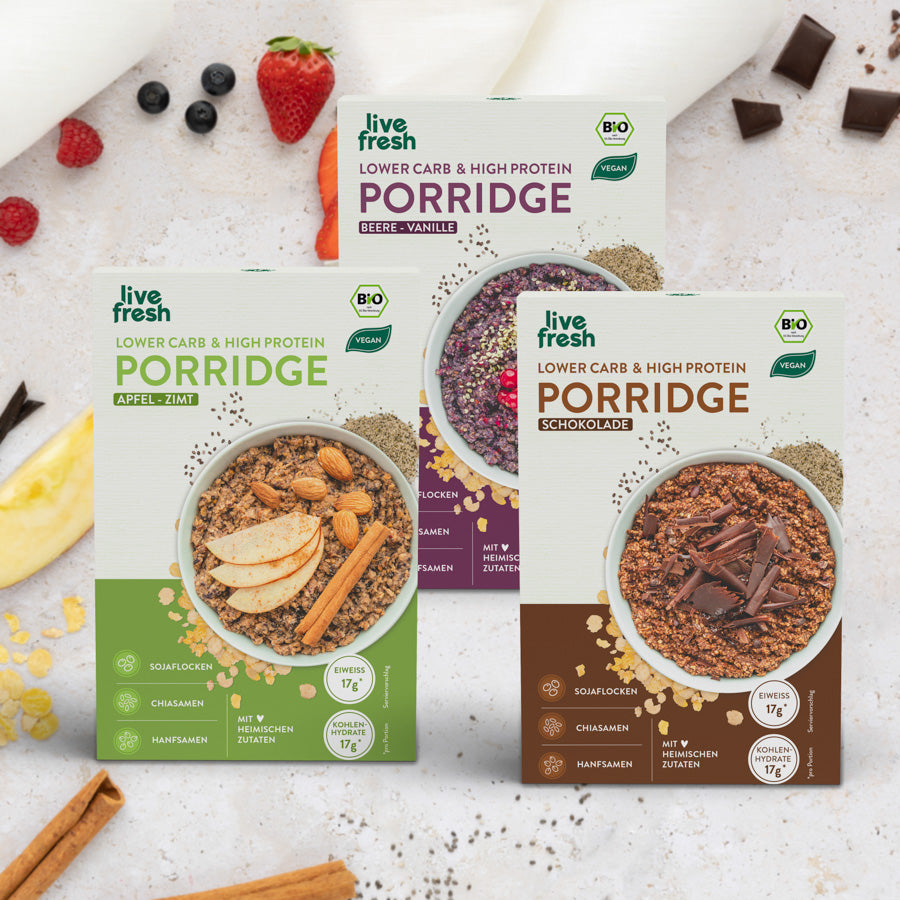 Packungen „Live Fresh“ Porridge in verschiedenen Geschmacksrichtungen: Apfel-Zimt, Beere-Vanille und Schokolade. Jede Packung betont, dass das Porridge „Lower Carb & High Protein“ ist, vegan und mit heimischen Zutaten hergestellt wird. Die Hauptzutaten wie Sojaflocken, Chiasamen und Hanfsamen werden hervorgehoben, und jedes Porridge enthält 17g Eiweiß und Kohlenhydrate. Um die Packungen herum sind passende Lebensmittel wie Beeren, Schokolade und Zimtstangen dekorativ arrangiert.