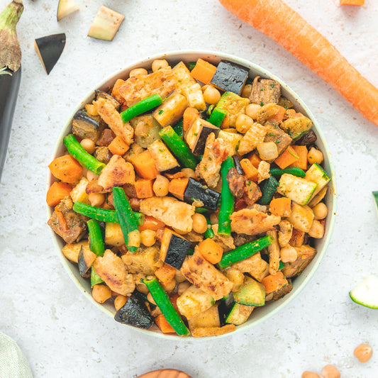 Eine Schüssel gefüllt mit einer bunten Mischung aus geröstetem Gemüse wie Auberginen, grünen Bohnen, Karotten, Zucchini und Kichererbsen, gewürzt nach der marokkanischen Ras el Hanout-Art.