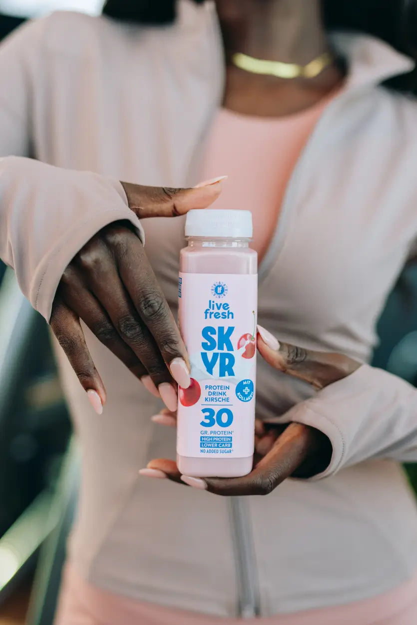 Nahaufnahme einer Hand die eine Flasche live fresh SK VR Protein Drink Kirsche mit 30 Gramm Protein vor dem Körper im Fitnessstudio hält.